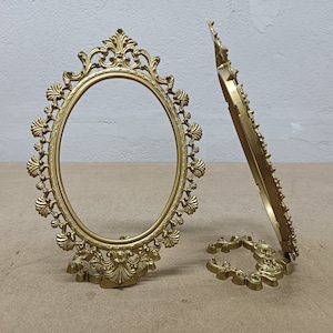 Peut inclure: Deux cadres photo ornés de couleur or avec des détails complexes. Les cadres sont de forme ovale et ont un support décoratif.