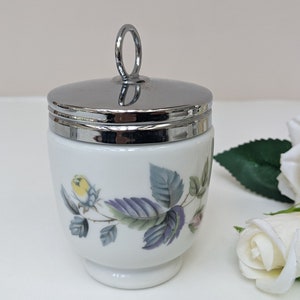 May include: A white porcelain egg coddler with a silver lid and a floral design. The coddler has a handle on the lid.