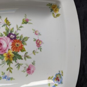 May include: A white rectangular serving dish with a floral design. The design features pink, yellow, red, and blue flowers with green leaves.