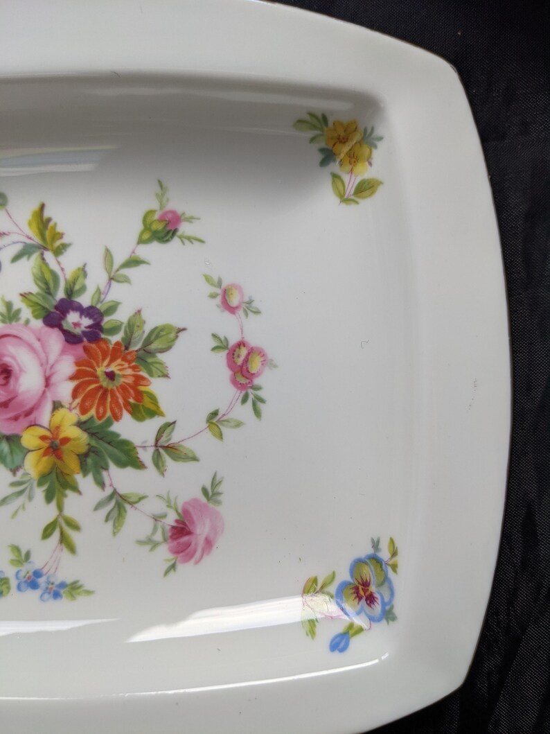May include: A white rectangular serving dish with a floral design. The design features pink, yellow, red, and blue flowers with green leaves.