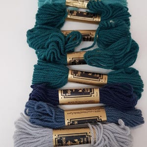 Pode incluir: Conjunto de 10 novelos de fio para bordar em tons de azul, verde e cinza. O fio &eacute; enrolado em carret&eacute;is de cart&atilde;o com etiquetas douradas que dizem "Tapisserie" e "100% Laine/Wool/Wolle/Lana".
