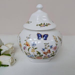 May include: White porcelain jar with a lid, decorated with a floral pattern and butterflies. The jar has a hexagonal base and a rounded body.