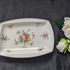 May include: A white rectangular serving platter with a floral design. The platter has a raised rim and a gold trim. The flowers are pink, yellow, and blue.