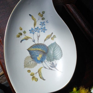 May include: A white ceramic serving dish with a blue and green floral design. The dish is shaped like a crescent moon and has a gold rim.