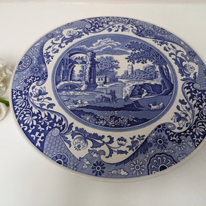 May include: Blue and white ceramic cake plate featuring a floral pattern and a central image of a landscape with a bridge and a building.