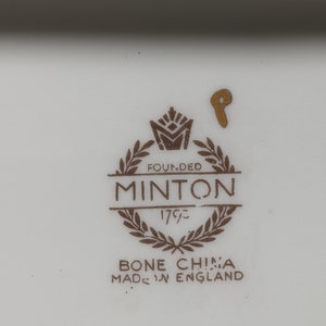 May include: A close-up of a brown and gold Minton bone china mark. The mark includes the words "Founded 1793" and "Bone China Made in England".