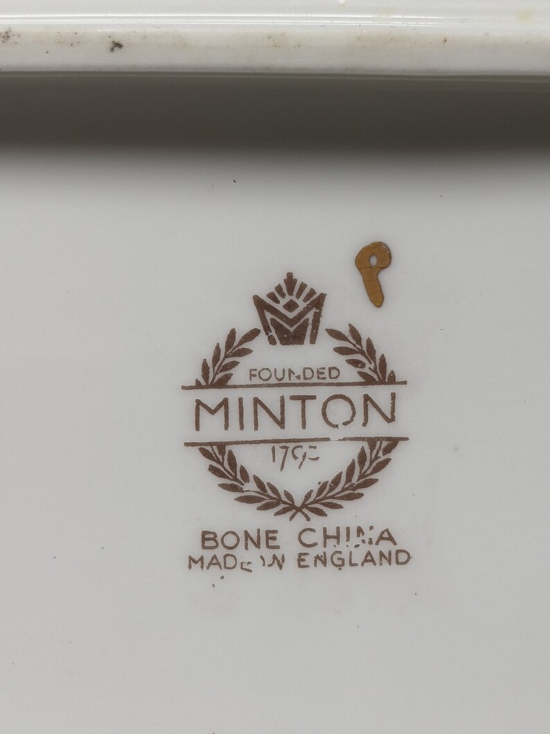 May include: A close-up of a brown and gold Minton bone china mark. The mark includes the words "Founded 1793" and "Bone China Made in England".