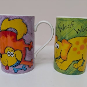 May include: Two ceramic mugs featuring dog illustrations. One mug is purple with a yellow and orange dog holding a bone. The other mug is green with a yellow dog with orange spots and the text "Woof Woof".