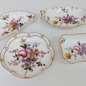 May include: Set of four small decorative dishes with floral patterns. The dishes are white with gold trim and feature a variety of colourful flowers.