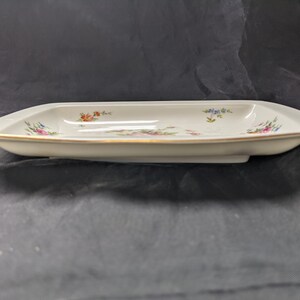 May include: A white rectangular serving dish with a gold rim and a floral design in shades of pink, blue, and orange.