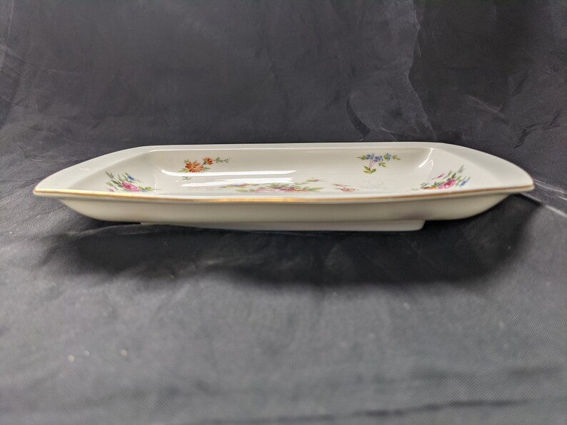 May include: A white rectangular serving dish with a gold rim and a floral design in shades of pink, blue, and orange.