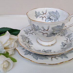 May include: A white teacup and saucer set with a silver and gold leaf design. The set has a delicate, scalloped edge.