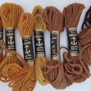 Pode incluir: Seis novelos de l&atilde; para tape&ccedil;aria de 10 mm em v&aacute;rios tons de marrom e laranja. A l&atilde; &eacute; etiquetada como "10mm Tapisserie Laine-Wool Wolle-Lana" com um n&uacute;mero em cada novelo.