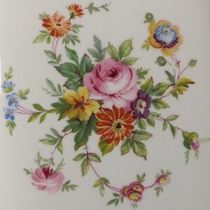 May include: A delicate floral design featuring a pink rose, yellow and orange flowers, and green leaves on a white background.