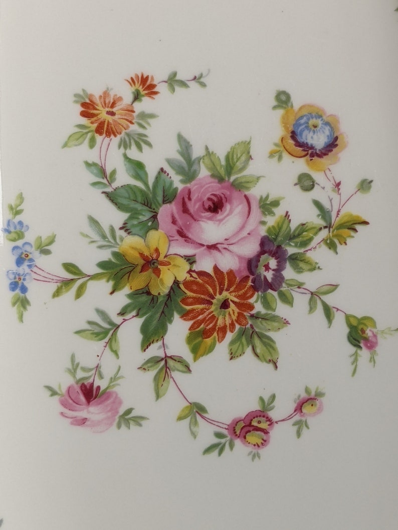May include: A delicate floral design featuring a pink rose, yellow and orange flowers, and green leaves on a white background.