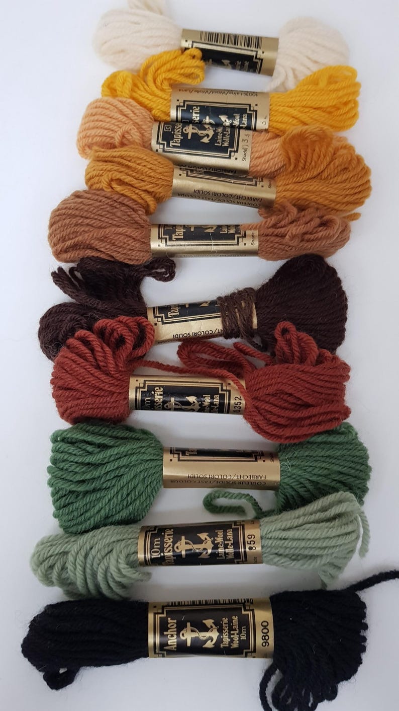 Pode incluir: Dez novelos de l&atilde; Anchor Tapisserie em v&aacute;rias cores, incluindo branco, amarelo, laranja, castanho, vermelho, verde e preto. Cada novelo &eacute; etiquetado com o logotipo da Anchor, "Tapisserie", "Wool-Laine" e o n&uacute;mero da cor.