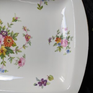 May include: White ceramic serving dish with a square shape and rounded corners. The dish is decorated with a floral pattern in shades of pink, yellow, orange, blue, and purple.