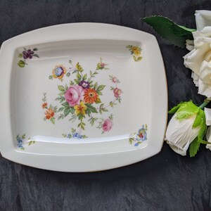 May include: A white rectangular serving dish with a gold rim and a floral design in shades of pink, yellow, orange, and blue.