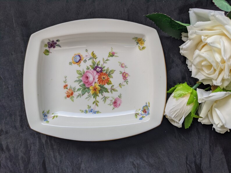 May include: A white rectangular serving dish with a gold rim and a floral design in shades of pink, yellow, orange, and blue.