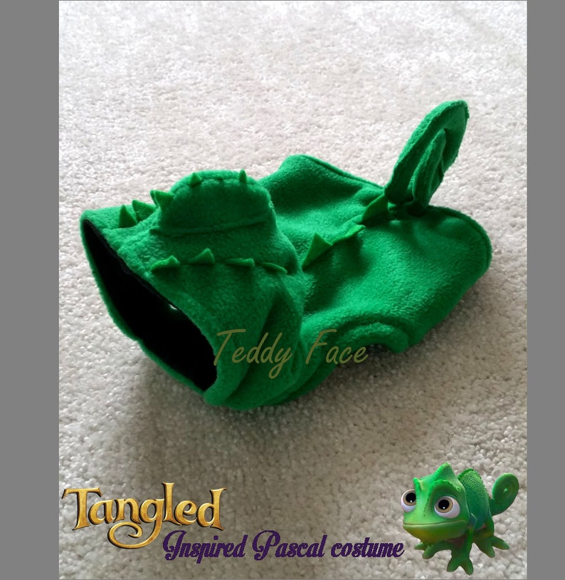 May include: A green fleece Pascal costume with a hood and tail, inspired by the character from the movie Tangled. The costume has a black interior and is decorated with triangular spikes. The text "Teddy Face" is visible on the costume.
