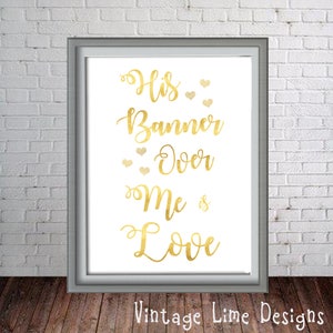 May include: Gold foil print with the text "His Banner Over Me is Love" with small hearts surrounding the text. The print is framed in a silver frame.