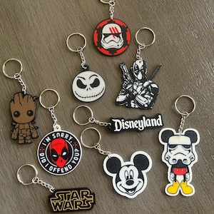 May include: A collection of nine character-themed keychains featuring various pop culture icons, including a brown tree creature, a white skull face, a red and black masked figure with the text I'M SORRY DID I OFFEND YOU, Star Wars, and Disneyland logos.