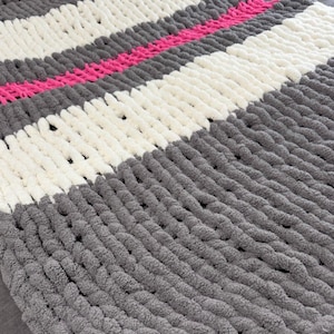 May include: A chunky knit throw blanket with stripes of gray, white, and pink yarn.