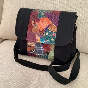 Schwarze Crossbody Stoff Umhängetasche nachhaltig handgefertigter verstellbarer Schultergurt bunte crazyquilt Details rotes Futter Messing Hardwear