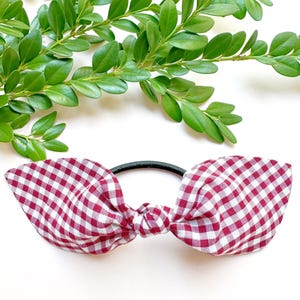 May include: A red and white gingham bow hair tie. The bow is tied in a knot and the hair tie is black.