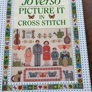 May include: A book cover titled "Jo Verso Picture It in Cross Stitch." The cover features a cross-stitch design with a family, pets, and various objects. The border is decorated with small cross-stitch images.