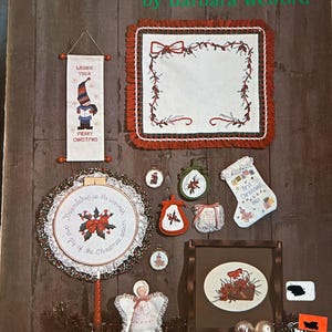 May include: A collection of Christmas-themed cross-stitch projects, including a banner with a gnome, a framed piece, ornaments, and a stocking. The projects feature red, green, and white colors, with the text "Christmas Crossing" at the top.