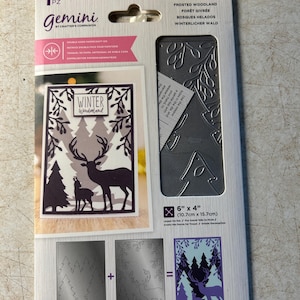 May include: A Gemini Create-a-Card die set for frosted woodland designs. The package includes a die for a winter wonderland card with a deer and tree silhouette. The die measures 6" x 4" (15.2cm x 10.1cm).