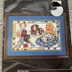 May include: Counted cross stitch pattern featuring five adorable puppies in various poses. The pattern includes a blue background, a red ball, and a patchwork quilt. The title of the pattern is "Pick Your Pup" and the size is 12 x 16 inches.