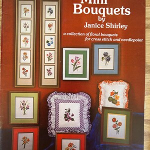 May include: A book titled "Mini Bouquets" by Janice Shirley, featuring a collection of floral bouquets for cross stitch and needlepoint. The cover features several framed embroidery designs with various flowers.