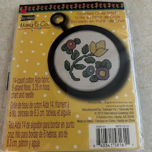 May include: A Mary & Co. counted cross stitch kit in a plastic package. The kit includes 14-count cotton Aida fabric, 6-strand floss, a 3.25 inch hoop, a chart, and a needle. The packaging features a yellow background with white polka dots.
