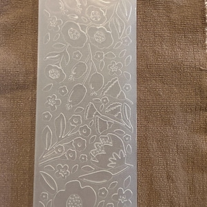 May include: A clear, rectangular Spellbinders embossing folder with a floral design. The design includes various flowers, leaves, and other botanical elements. The folder is marked with "SPELLBINDERS" and "SES-017".