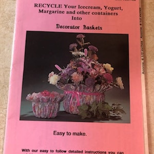 May include: A pink pamphlet with the title "RECYCLE Your Icecream, Yogurt, Margarine and other containers Into Decorator Baskets". The pamphlet shows a pink and white floral arrangement in a pink and white woven basket. The text "Easy to make." is below the image.