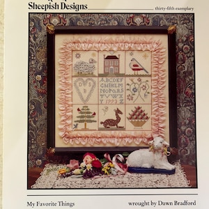 May include: A cross-stitch pattern featuring a framed design with a variety of motifs, including a house, a bird, a heart, a tree, a deer, and a basket of fruit. The pattern is titled "My Favorite Things" and is attributed to Dawn Bradford. The pattern is part of a collection called "Sheepish Designs."