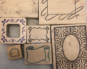 May include: Set of seven wooden rubber stamps with different designs. The stamps feature various frames, borders, and swirls. The stamps are made of natural wood and have a light brown color.