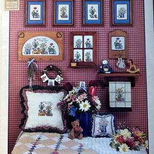May include: A cross-stitch pattern booklet featuring a floral theme with the title "Love Makes Things Grow". The cover shows a variety of cross-stitch designs, including a floral wreath, a window with flowers, and a pillow with the phrase "Love makes things grow".