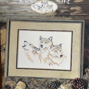 May include: Cross-stitch pattern featuring three wolves howling at the moon. The pattern is titled "All For One" and is from StitchWorld X-Stitch. The pattern is framed in a brown wood frame.