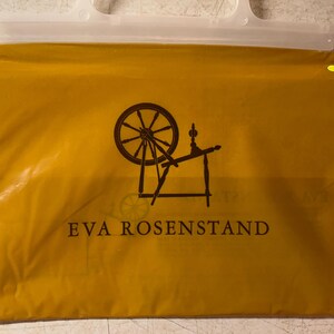 May include: A yellow plastic bag with a white handle and a black silhouette of a spinning wheel with the text "EVA ROSENSTAND" printed on the front.