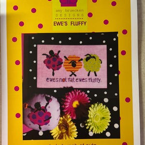 May include: A cross-stitch pattern featuring three sheep with the text "ewes not fat ewes fluffy." The pattern is surrounded by a black and white polka dot border. The image is on a yellow background with pink polka dots.