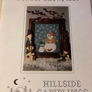 May include: A cross stitch pattern featuring a snowman with a red cardinal and the text "Let-her Snow, too!" The pattern is titled "Hillside Samplings" and includes the text "Designs by Lesley Rudnick".