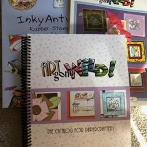 May include: Three spiral bound books with the title "Art Gone Wild! The Catalog for Papercrafters" on the front cover. The books are on a white surface. The book on the left has the title "Inky Antics Rubber Stamps" on the front cover. The book on the right has the title "Art Gone Wild!" on the front cover.