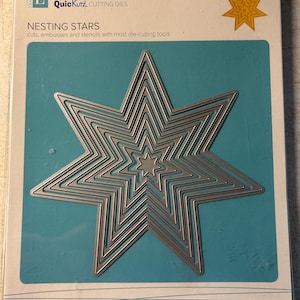 May include: Quickutz Nesting Stars cutting dies. The package features a set of seven nested star-shaped dies in silver metal. The dies are displayed on a teal background, with the product name and description printed on the packaging. The packaging is clear plastic.