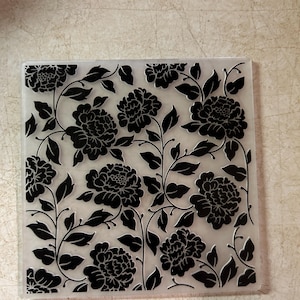 May include: Clear plastic sheet with a black floral pattern of leaves and flowers. The design is a repeating pattern of large flowers and smaller leaves.