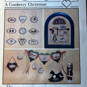 May include: A cross-stitch pattern booklet titled "HeartStrings: A Cranberry Christmas" by Pat Thode. The booklet features a variety of holiday-themed designs, including ornaments, a rocking horse, and a Santa Claus figure.