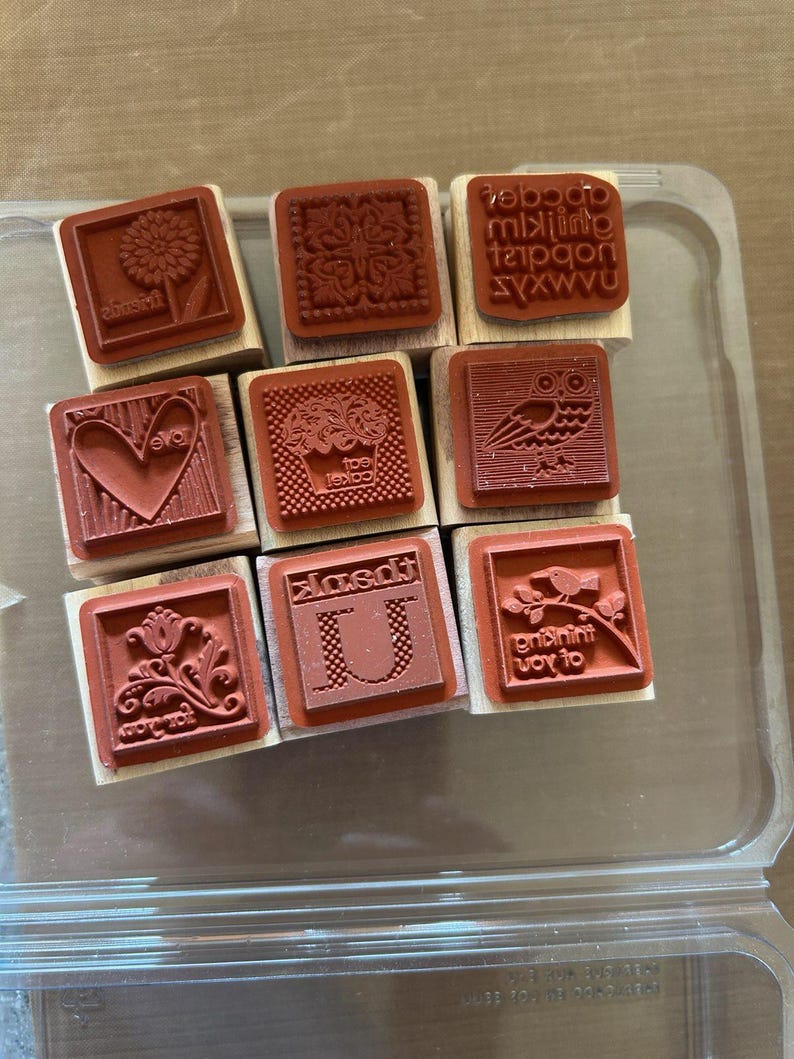 May include: A collection of nine red rubber stamps with wooden blocks. Designs include a sunflower, a heart, an owl, a floral pattern, a cupcake, and the letter "U". Some stamps have text, including the words "love" and "joy to".