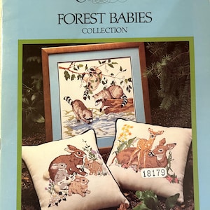 May include: A cross-stitch pattern booklet for a Forest Babies collection. The cover features three cross-stitch designs: a raccoon family, a deer family, and a rabbit family. The booklet is titled "Something Special Forest Babies Collection" and includes the text "Designs by Candi Martin".